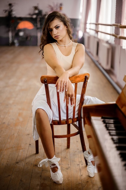 Pretty young dancer girl is sitting at the piano in the dancing studio