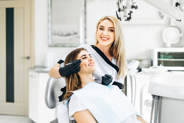 Pretty young female dentist making examination and treatment for young female patient in dental clinic.