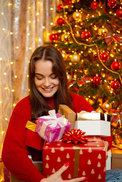 Pretty young girl in bright red sweater with many presents in Christmas morning