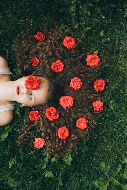 Pretty young girl laying at the grass with flowers in her curly scattered long hair