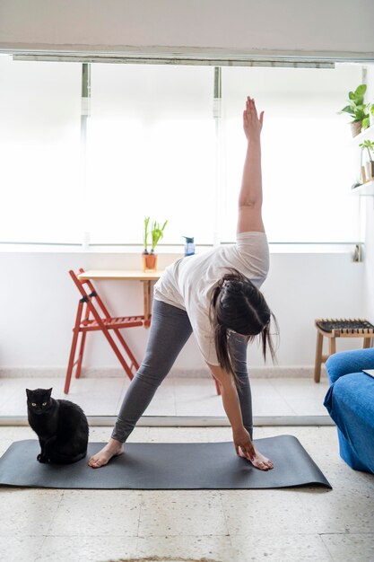 pretty young girl practicing exercise and yoga in her living room with a black cat