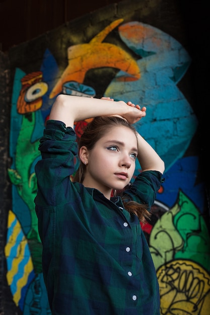 Pretty young girl in street style checkered shirt in front  graffiti wall. Urban 