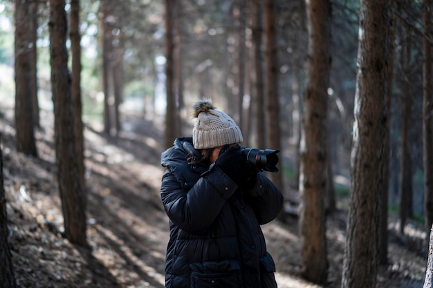 pretty young girl in warm clothes walking through a forest taking photos