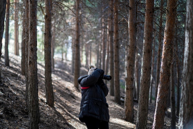 pretty young girl in warm clothes walking through a forest taking photos