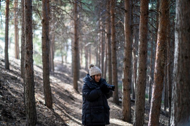 pretty young girl in warm clothes walking through a forest taking photos