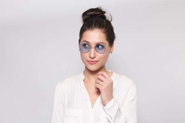 Pretty young girl in white blank t-shirt, wearing glasses, empty wall, studio portrait