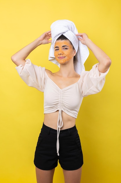 A pretty young girl with a scrub mask on her face poses for the camera and smiles against a yellow background