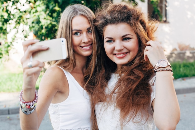 Pretty young girls doing selfie outdoor on the street in summer girls have fun with smartphone doing selfie