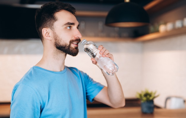 Pretty young man with beard drinking fresh water in bottle