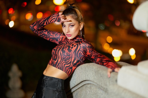 Pretty young model with long straight hair poses in tight clothes at night in the streets of Madrid Spain