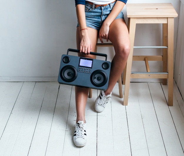 Pretty young sexy tanned girl posing in summer in white studio with hi-fi modern tape recorder