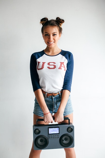 Pretty young sexy tanned girl posing in summer in white studio with hi-fi modern tape recorder