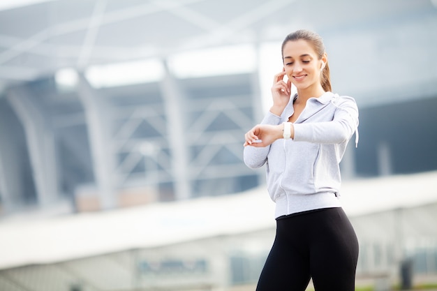 Pretty young sportswoman putting on headphones and listening to music in city