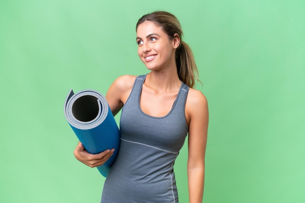 Pretty Young Uruguayan sport woman going to yoga classes while holding a mat over isolated background thinking an idea while looking up