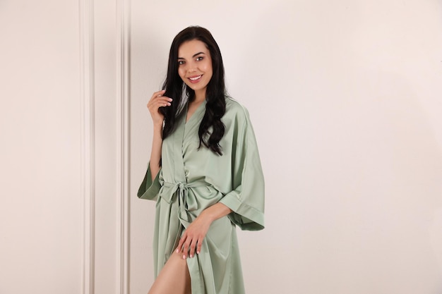 Photo pretty young woman in beautiful light silk robe near white wall