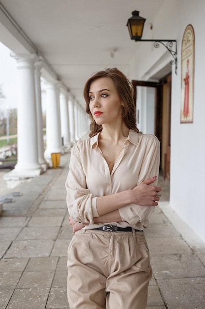 Pretty young woman in beige blouse seductive red lipstick and wavy hair standing on veranda of cafe