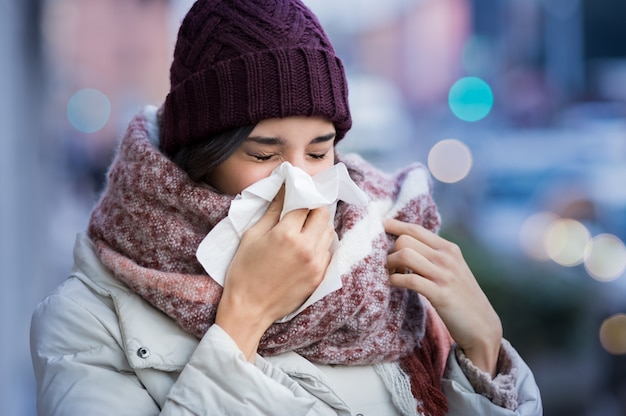 Pretty young woman blowing her nose with a tissue outdoor in winter