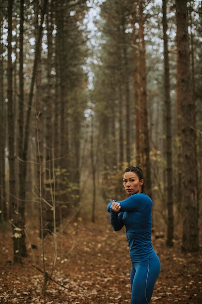 Pretty young woman in blue track suit stretching before workout in the autumn forest