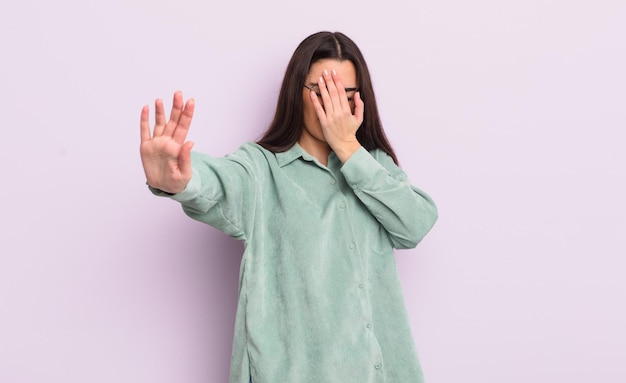 Pretty young woman covering face with hand and putting other hand up front to stop camera refusing photos or pictures