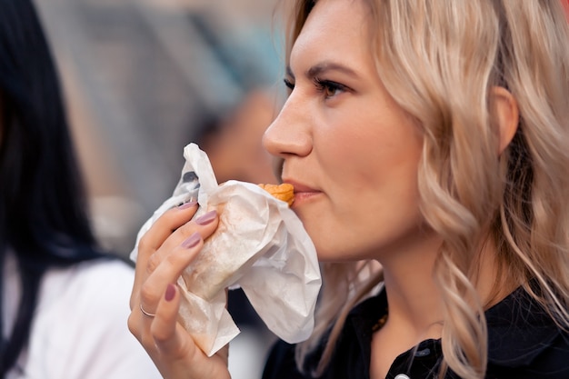 Pretty young woman eating hamburger outdoor on the street.