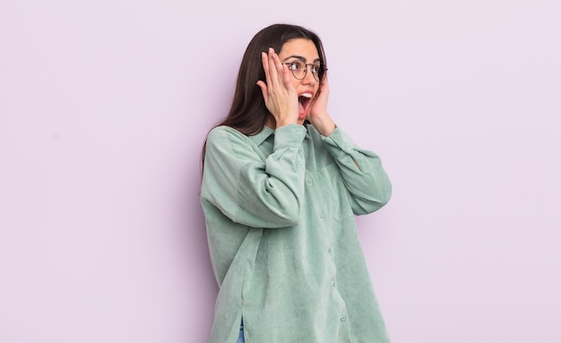 Pretty young woman feeling happy excited and surprised looking to the side with both hands on face