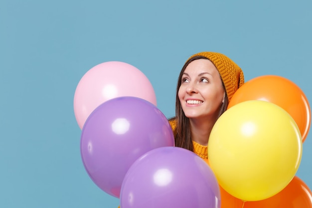 Pretty young woman girl in sweater and hat posing isolated on blue background. Birthday holiday party, people emotions concept. Mock up copy space. Celebrating hold colorful air balloons looking up.