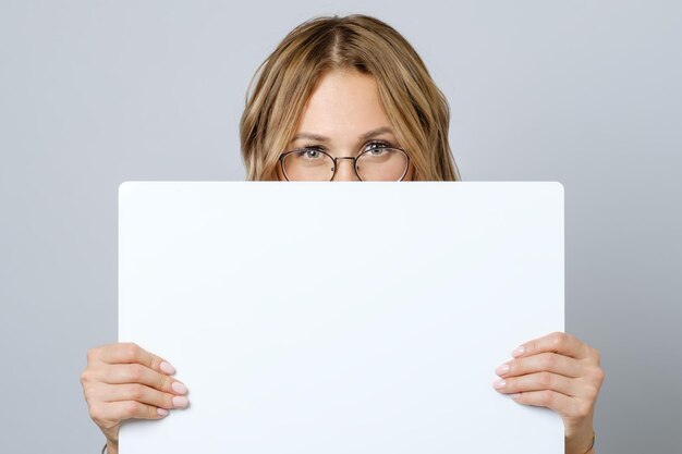 Pretty young woman holding empty blank board isolated on the gray background