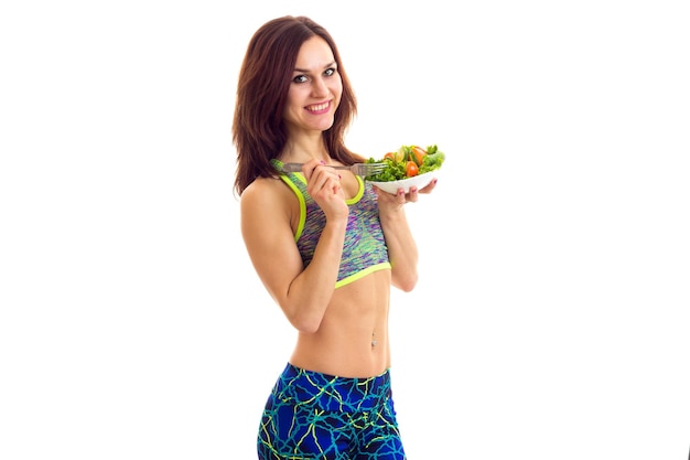 Pretty young woman holding white plate with green salad and tomato on white background in studio