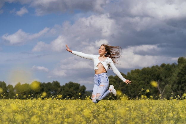 Pretty young woman jumping happy in a field of yellow flowers