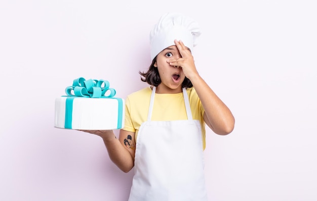 Pretty young woman looking shocked, scared or terrified, covering face with hand. chef cooking a cake