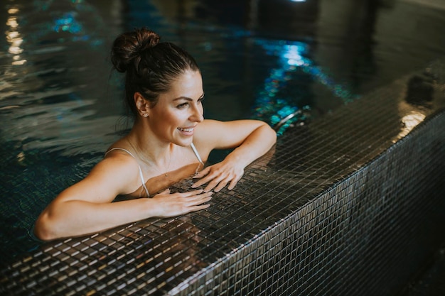 Pretty young woman relaxing on the poolside of indoor swimming pool