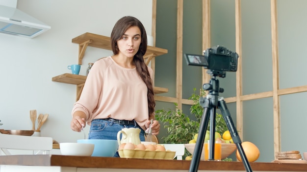 A Pretty Young Woman Shooting a Blog About Cooking. Video Blog of Healthy Food. Attractive Woman is Cooking on the Camera. Woman is Streaming Online Video Vlog.Girl Conduct Remote Teaching to Cooking