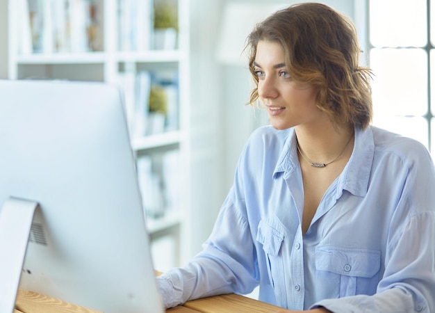 Pretty young woman sitting at desk and typing on laptop