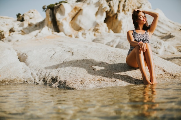 Photo pretty young woman sitting on the rocky shore by sea