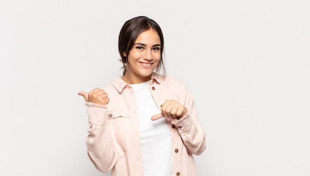 Pretty young woman smiling cheerfully and casually pointing to copy space on the side, feeling happy and satisfied