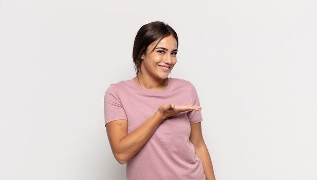 Pretty young woman smiling cheerfully, feeling happy and showing a concept in copy space with palm of hand