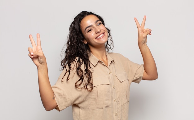 Pretty young woman smiling and looking happy, friendly and satisfied, gesturing victory or peace with both hands