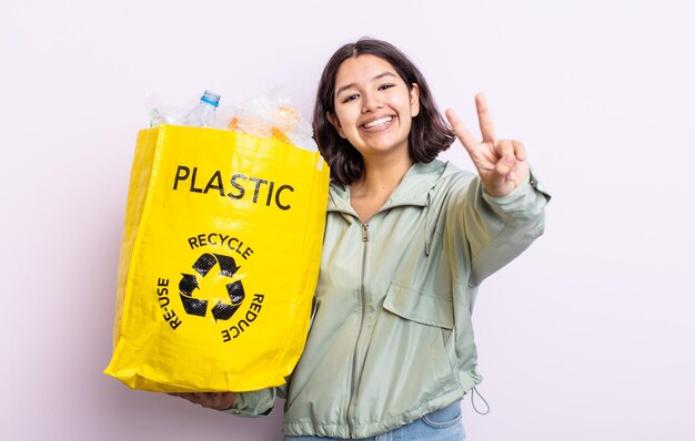 Pretty young woman smiling and looking happy, gesturing victory or peace. plastic recycling concept