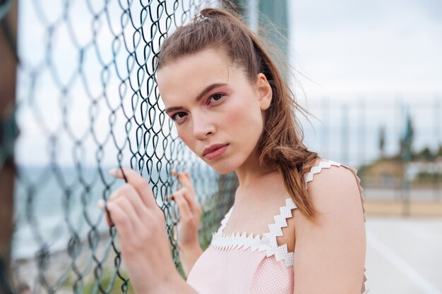 Pretty young woman standing outdoors near chain link fence