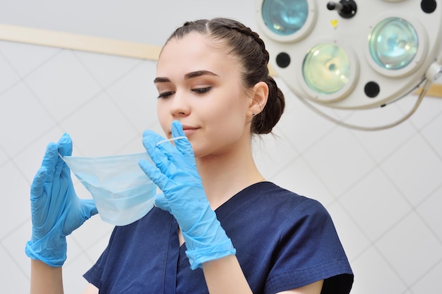 Pretty young woman in a surgical suit puts on a sterile mask