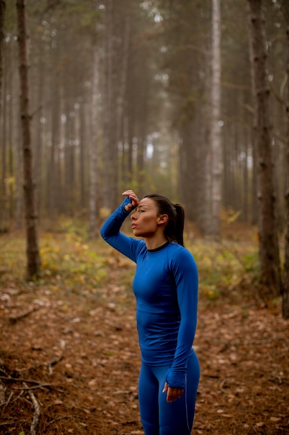 Pretty young woman take a break during outdoor exercise on the forest trail at autumn