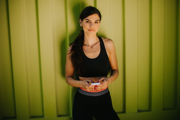 Pretty young woman taking a break during exercising outside and using mobile phone