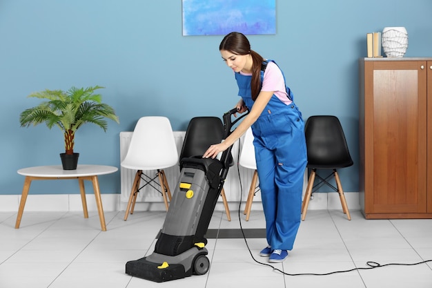 A pretty young woman in uniform vacuuming the floor at the office