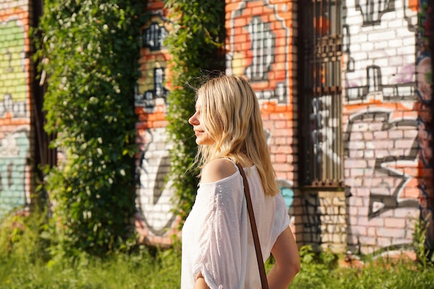 Pretty young woman with blond hair standing on a street with the graffiti wall