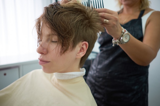 Pretty young woman with closed eyes relaxing at the hairdresser salon. Hairstylist serving client at barber shop or beauty salon.