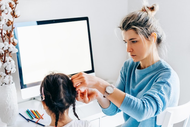 Pretty young woman with daughter sitting at home and working Young mother with toddler child working at the computer and is distracted by the kid Housewife sitting with her child and working