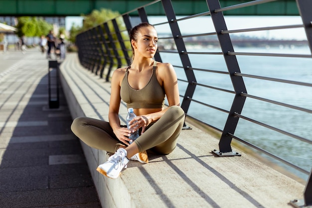 Pretty young woman with earphones takes a break after running in urban area