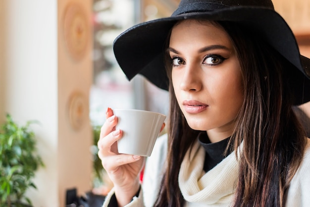 Pretty young woman with hat drinking coffee