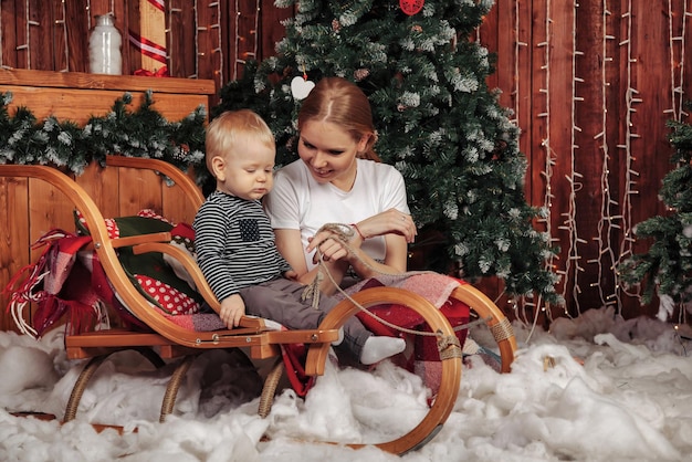 Pretty young woman with oneyearold child playing by Christmas tree