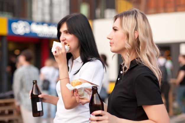 Pretty young women eating hamburger outdoor on the street.